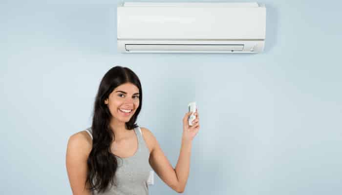 Woman Holding Remote Control In Front Of Air Conditioner